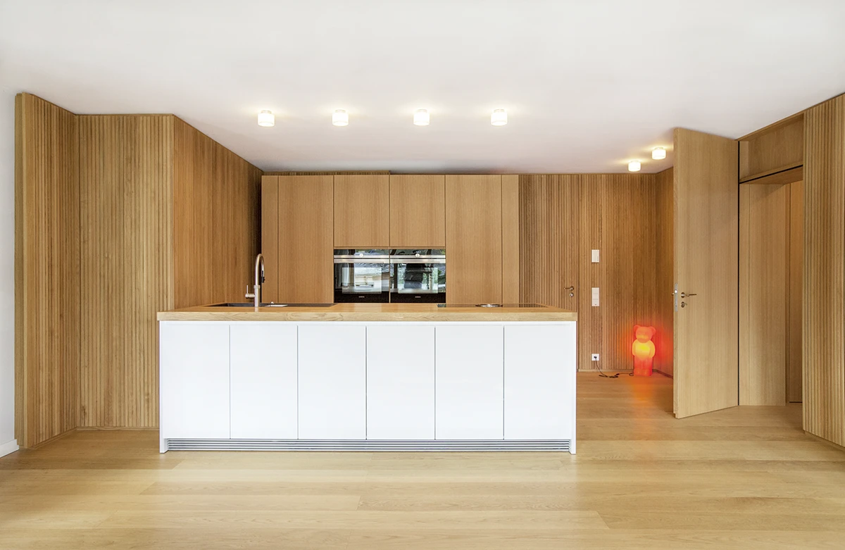 Blick auf die moderne Küche, Wände in Holzstab-Optik, weisse Fronten, Holzboden