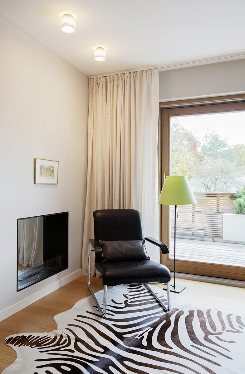 Wohnbereich mit Fernseher und elegantem Sessel in schwarz auf dem Holzboden ein Zebrafell-Imitat