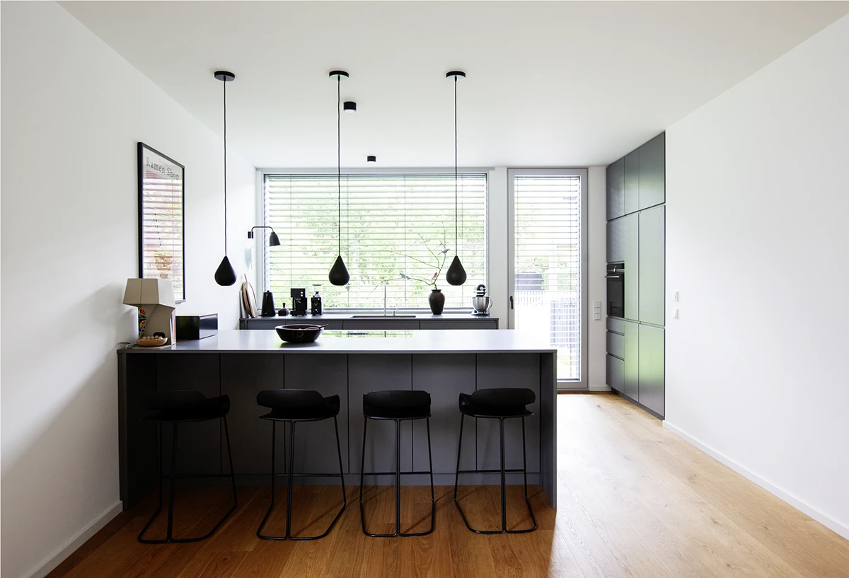 stoiber-architektur-neubau-einfamilienhaus_muenchen-kueche_07 Küche mit Thekenelement und Lichtpendeln, große Fensterwand, Holzboden, Wände weiss