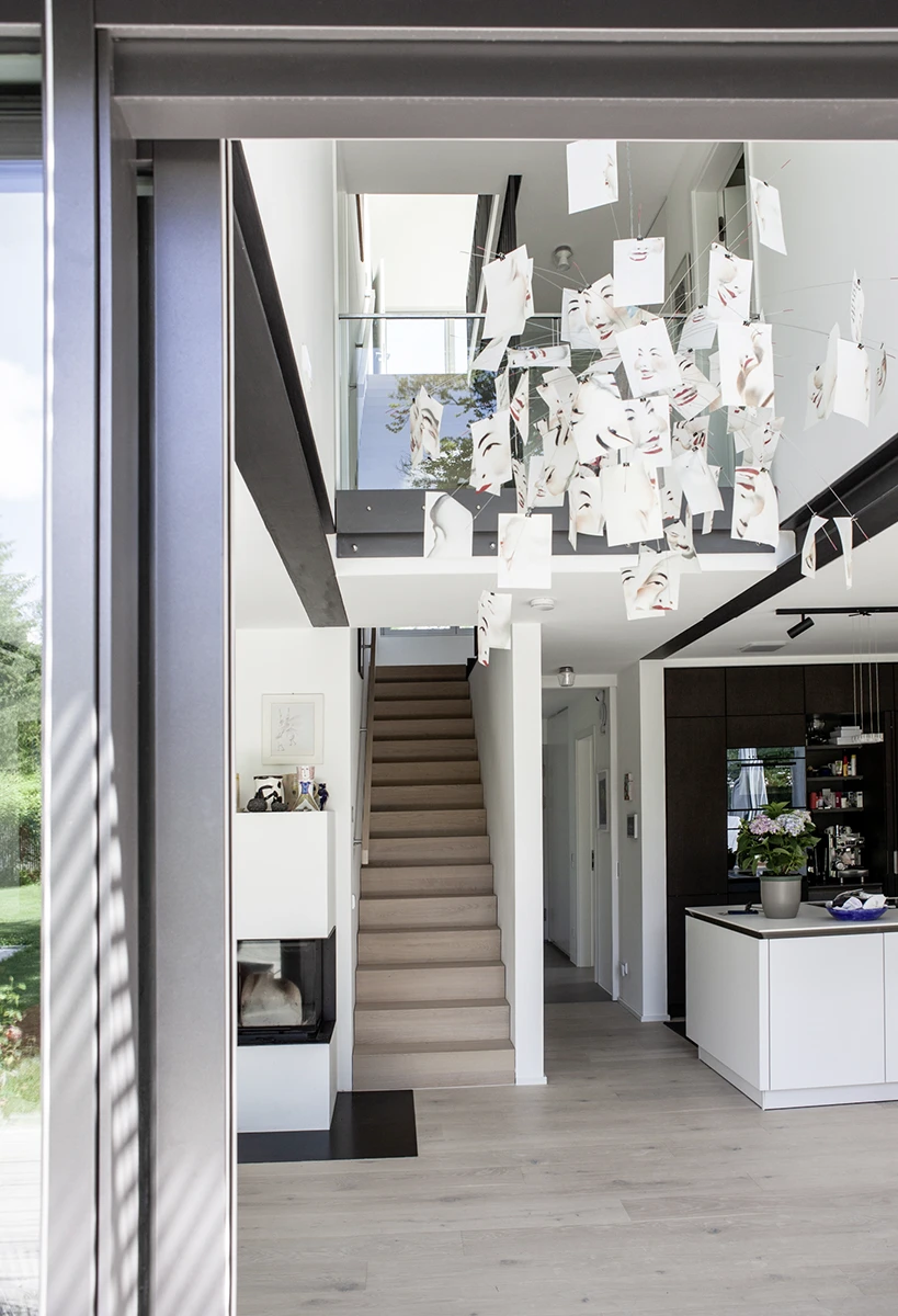 Erdgeschoss mit Blick die Treppe hoch, links in die Wand eingelassener geschlossener Kamin, rechts Küche, heller Holzboden, nach oben offene Architektur