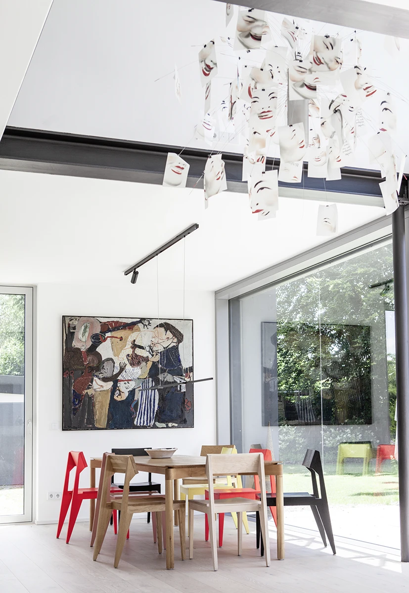 Blick auf den Essbereich, nach oben offene Architektur in die darüber liegenden Stockwerke, Kunst an einer Wand, rechts Blick durch die Fensterfront in den Garten