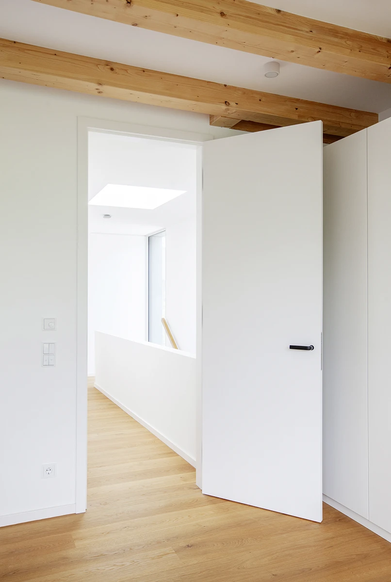 stoiber-architektur-neubau-einfamilienhaus_muenchen_flur_11 Flur mit Sichtbalkendecke, Blick durch eine Tür in das helle Treppenhaus, Wände weiss