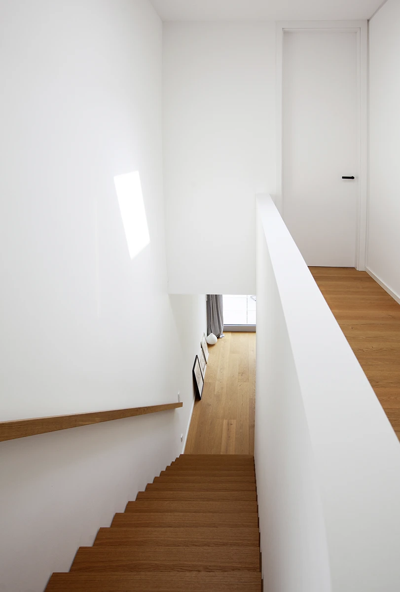 stoiber-architektur-neubau-einfamilienhaus_muenchen_treppe_09 Blick Trepp runter in das Erdgeschoss, Treppenstufen mit dunklem Holz, weisse Wände