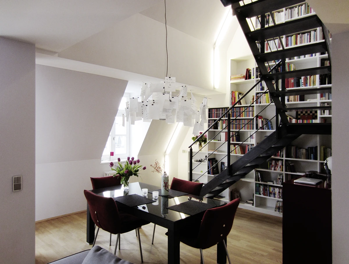 Blick auf den Essbereich mit dunkle Tisch und vier lilafarbenen Stüchlen, der Treppe und dem Bücherregal in Hintergrund
