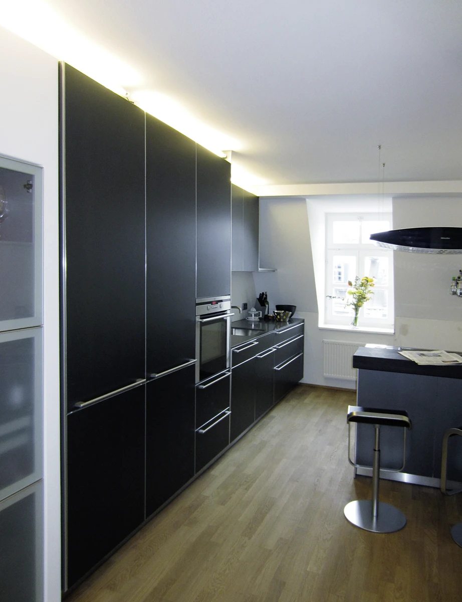 Blick in die moderne Küche mit dunklen Fronten, Holzfussboden und Esstheke, Fenster