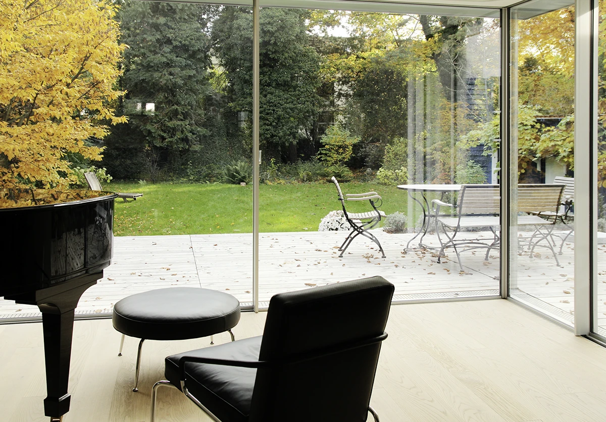 stoiber-architektur_sanierung-einfamilienhaus-anbau_muenchen-obermenzing_wohnen-terasse_06 Blick aus dem Wohnzimmer durch die Glasfront auf die Terasse, im Vordergrund die Ecke eines Flügels