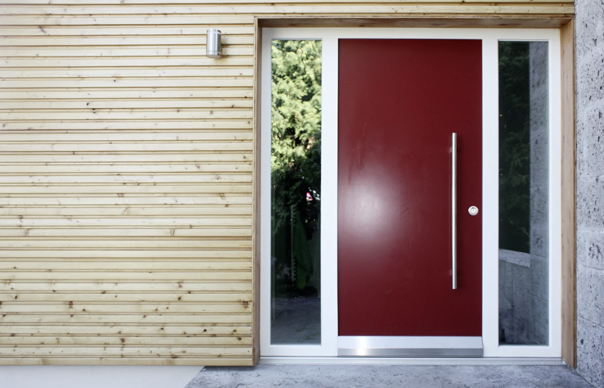 stoiber-architektur_sanierung-einfamilienhaus_muenchen_eingangsbereich_03 Eingangsbereich mit roter moderner Tür, schmale türhohe Fenster links und rechts der Tür, Fassade mit Holz verkleidet