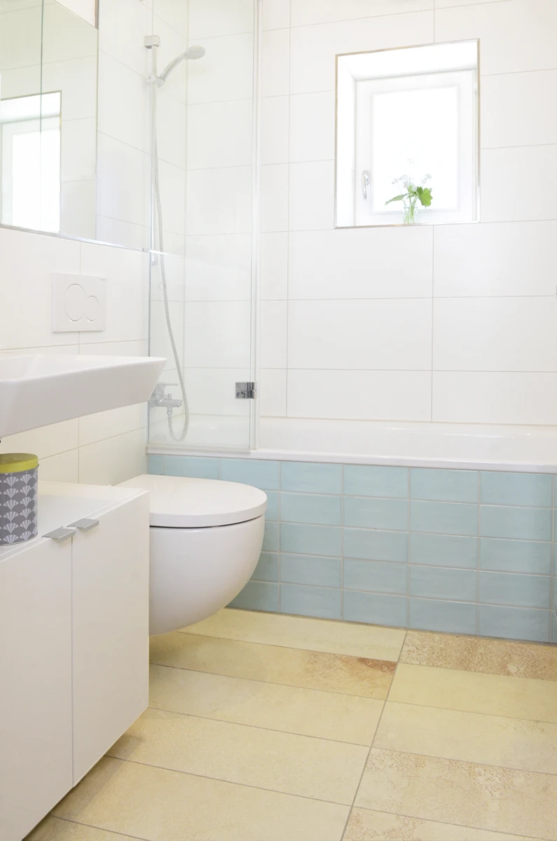 stoiber-architektur_sanierung_muenchen_badezimmer_10 Neu renoviertes Badezimmer, modern, beige gefliester Boden, Bademöbel und Wände in weiß, Badewannensockel in Hellblau,