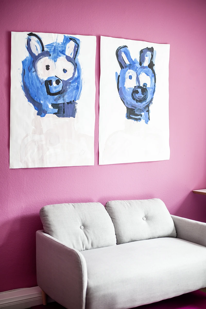 Sofa vor Magenta farbenen Wand mit zwei Bildern.