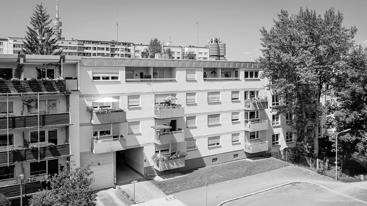 stoiber-architektur-muenchen-2026-sanierung-brunnerstr-bestand-04 Schwarz-Weiß-Foto des Wohnhauses vor der Sanierung mit Flachdach, Betonbalkonen, Rollläden und Durchfahrt