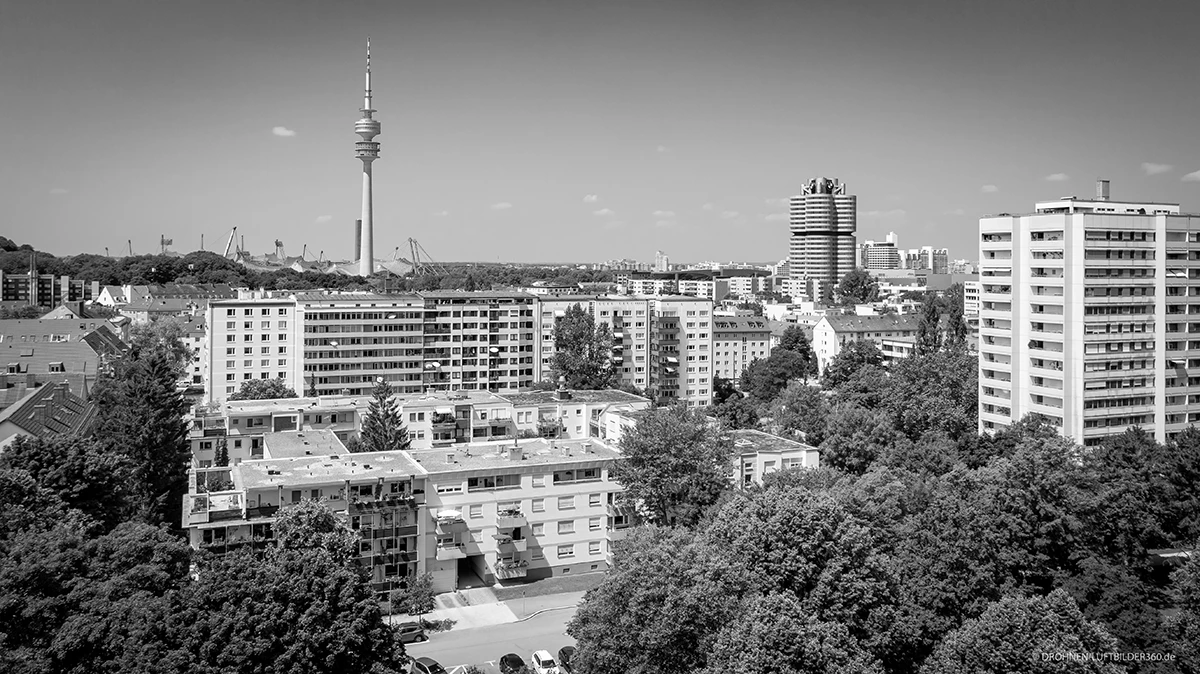 stoiber-architektur-muenchen-2026-sanierung-brunnerstr-bestand-05 Schwarz-Weiß-Luftbild eines Wohnviertels in München-Schwabing mit Olympiaturm und BMW-Hochhaus im Hintergrund