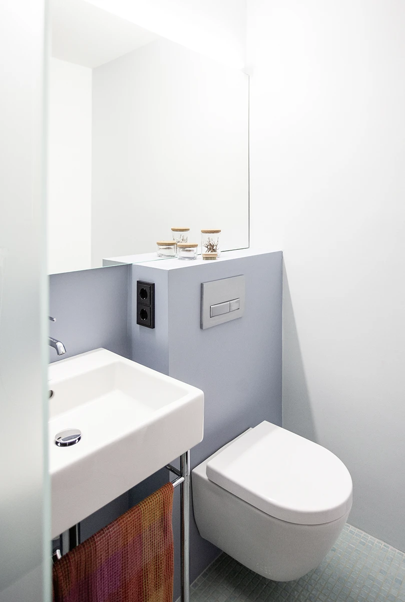 stoiber-architektur-muenchen-2026-sanierung-gudrunstr-07 Kleines Bad mit Waschbecken, wandhängendem WC, hellblauer Vorwand und großem Spiegel